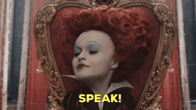 the queen of hearts from alice in wonderland is sitting in a heart shaped chair and saying speak !