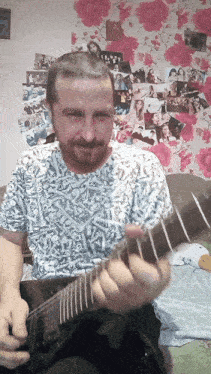 a man playing a guitar in front of a wall with pictures of people