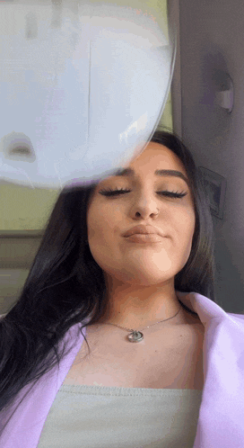 a woman wearing a necklace and a purple jacket looks down at something
