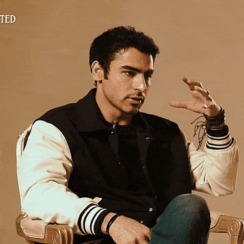 a man wearing a black and white jacket is sitting in a chair with the word ted behind him