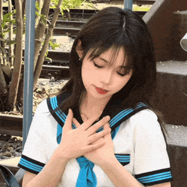 a girl in a school uniform with a blue tie holds her hands on her chest