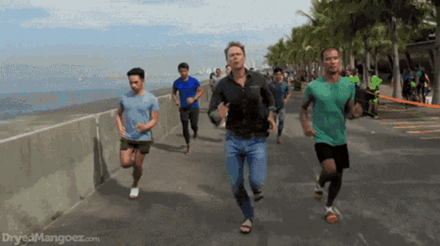 a group of men are running on a sidewalk and the website dryedmangoez.com is on the bottom