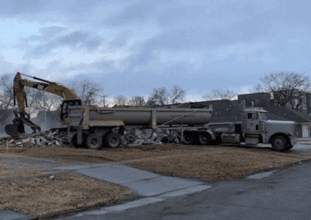 a dump truck with a yellow excavator on the back is parked in a yard