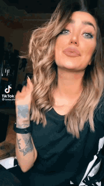 a woman with a tattoo on her arm is taking a selfie with a tiktok app on her phone