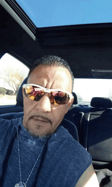 a man wearing sunglasses and a necklace is sitting in a car