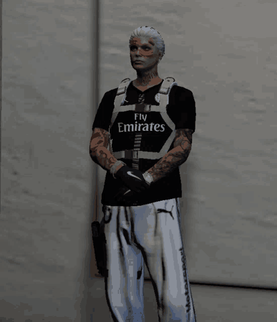 a man wearing a fly emirates shirt stands in front of a white wall