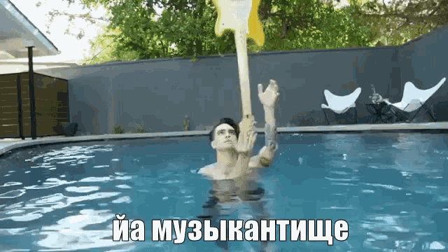 a man is floating in a pool holding an inflatable guitar with russian writing behind him