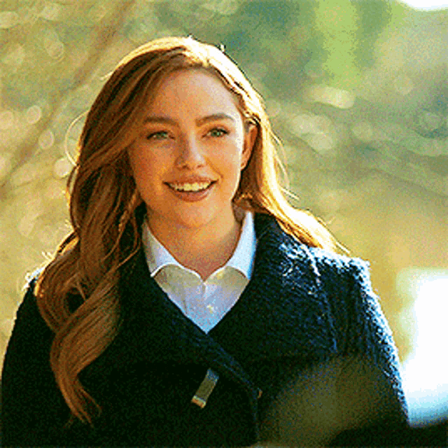 a woman wearing a blue coat and a white shirt is smiling for the camera .