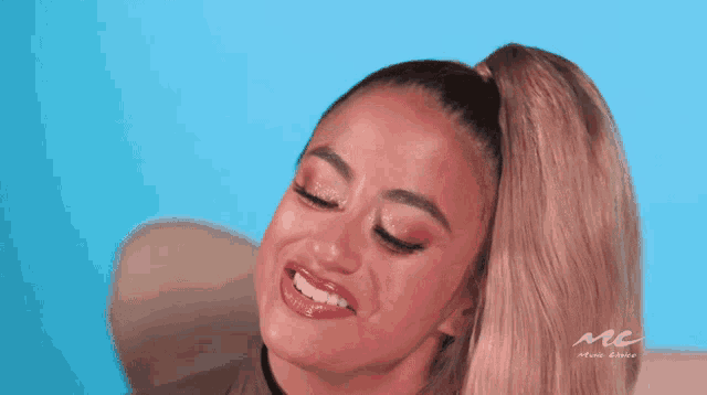 a woman with a ponytail is smiling in front of a blue background with the letters mc on it