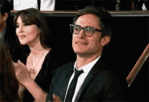 a man in a suit and tie is sitting next to a woman in a black dress applauding .