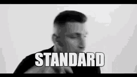 a black and white photo of a man making a hand gesture with the word standard written on it .