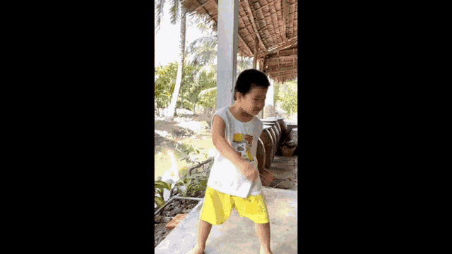a young boy in a white tank top and yellow shorts is standing on a porch .