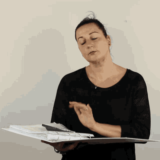 a woman in a black shirt is holding a folder with papers in it