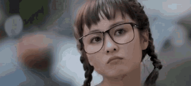 a woman wearing glasses and pigtails is looking at the camera .