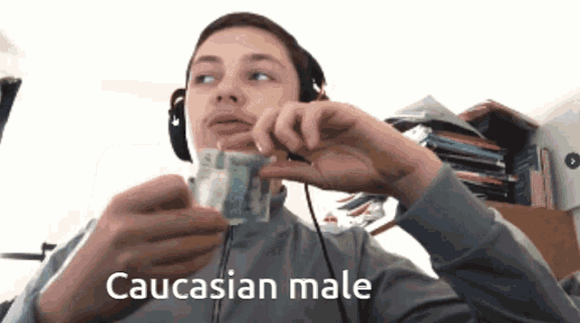 a caucasian male wearing headphones holds a dollar bill in his hand