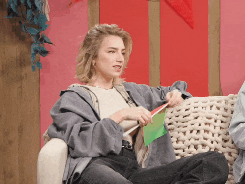 a woman is sitting on a couch holding a green piece of paper