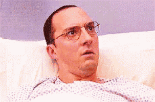 a man wearing glasses is laying in a hospital bed with a surprised look on his face .