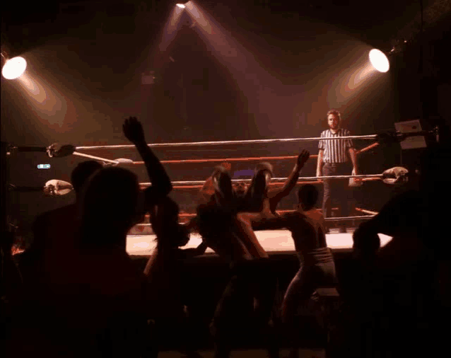 a referee stands in the middle of a wrestling ring watching two men fight