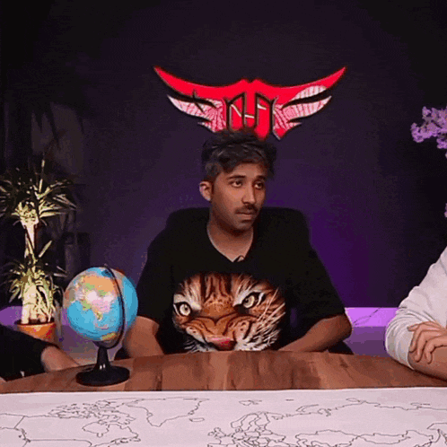 a man wearing a tiger t-shirt sits at a table with a globe on it