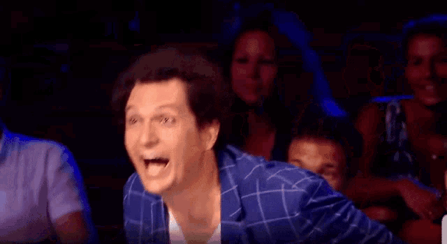 a man in a blue jacket is laughing while sitting in front of a crowd .