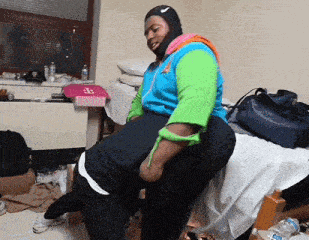 a man wearing a nike hat sits on another man 's lap in a room