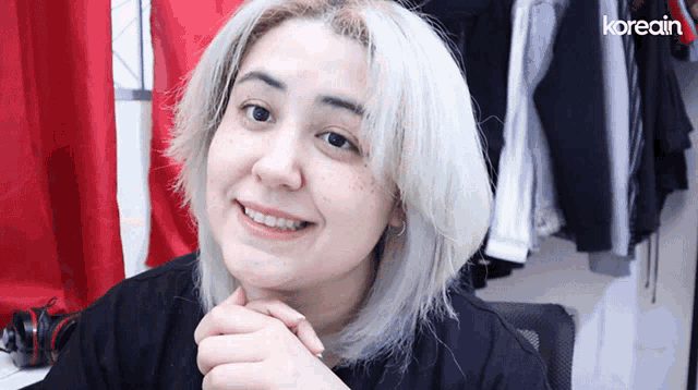 a woman with white hair is smiling in front of a clothes rack with the word koreain on the bottom