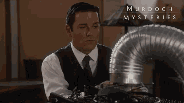a man in a suit and tie stands in front of a murdoch mysteries sign