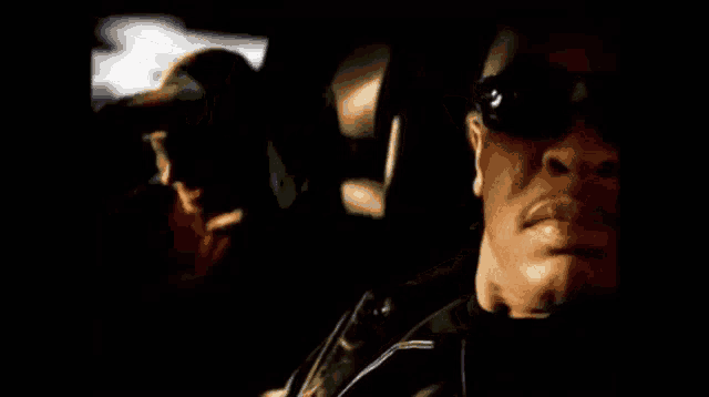 a man wearing sunglasses is sitting in a car next to another man .
