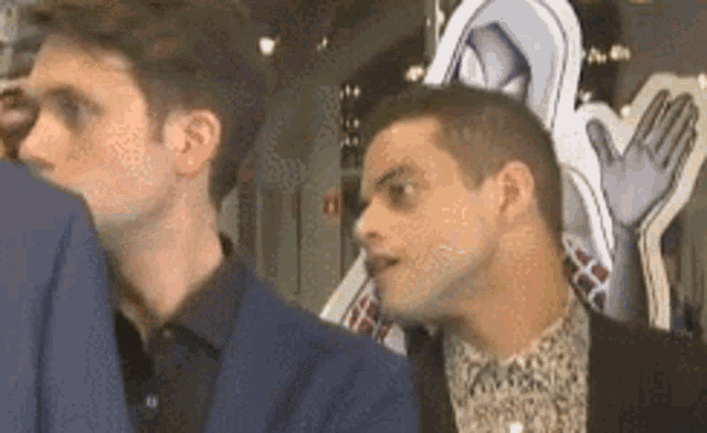 a man in a suit and a man in a plaid shirt are standing next to each other and talking .