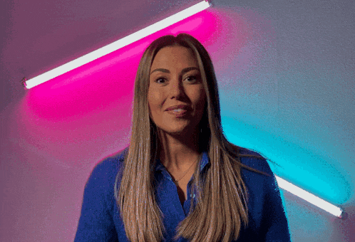 a woman in a blue shirt stands in front of a pink and blue light