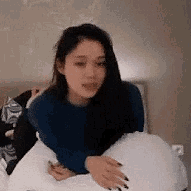 a woman is laying on a bed holding a pillow and making a funny face .