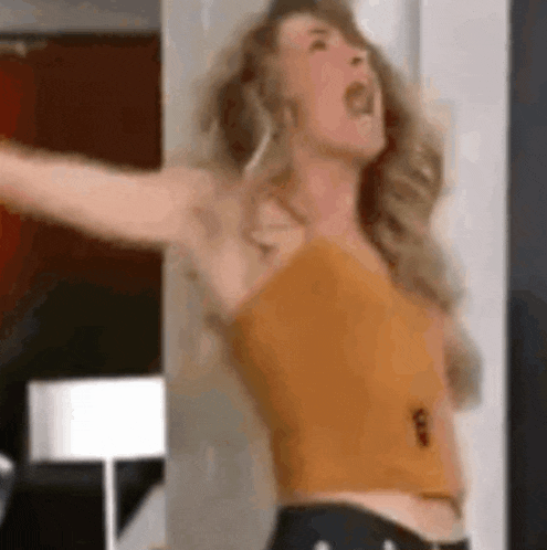 a woman in a yellow tank top is standing with her arms outstretched .