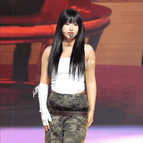 a woman in a white tank top and camo pants stands on a stage