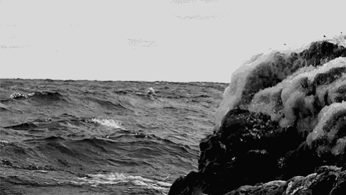 a black and white photo of waves crashing against a rocky shoreline