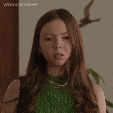 a woman in a green sweater says okay in front of her face