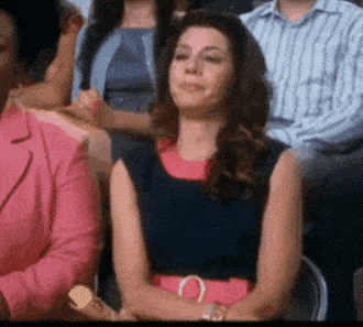 a woman in a pink dress is sitting in a crowd of people with her eyes closed .