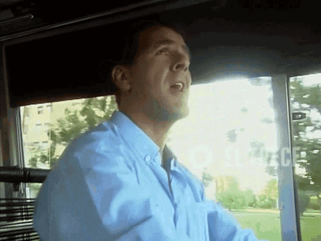 a man in a blue shirt is singing into a microphone while driving a bus