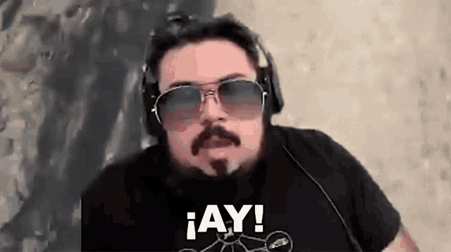 a man with a beard and sunglasses is wearing headphones and saying ay .