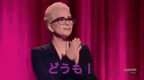 a woman wearing glasses and a black suit is clapping her hands on a stage .