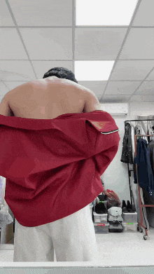a shirtless man is taking off a red jacket
