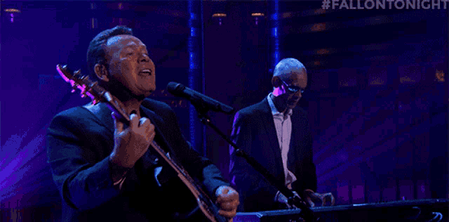 a man singing into a microphone while another man plays keyboards
