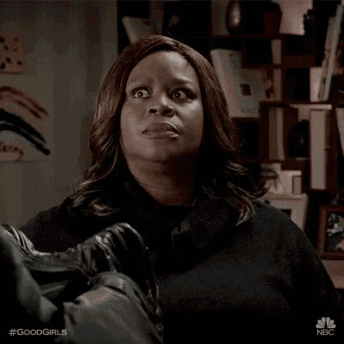 a woman in a black sweater is holding a pair of shoes and making a surprised face .