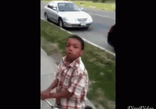 a young boy in a plaid shirt is riding a bike on a sidewalk in front of a white car