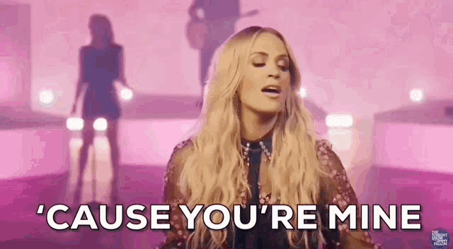 a woman is singing a song on a stage and the words `` cause you 're mine '' are coming out of her mouth .