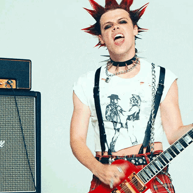 a man with a mohawk is playing a guitar in front of an amplifier