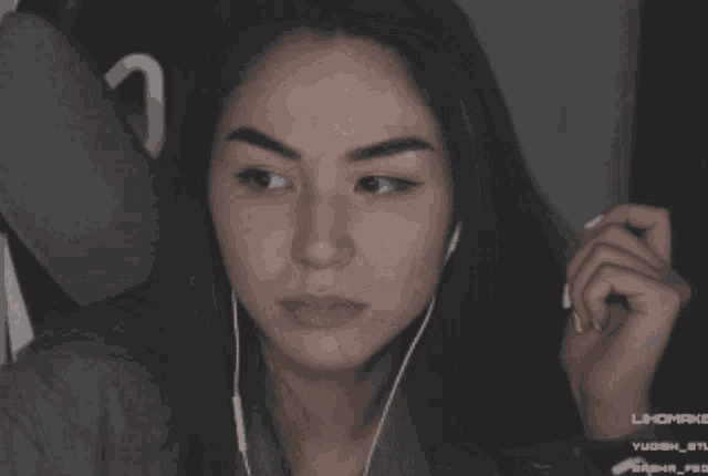 a woman wearing ear buds looks at the camera with a screen behind her that says lhcmake