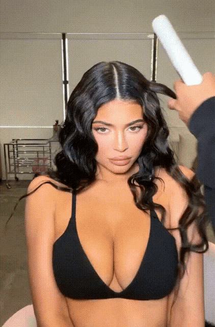 a woman in a black bikini top is getting her hair styled