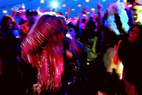 a woman with pink hair is dancing in front of a crowd at a party