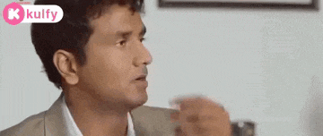 a man in a suit and white shirt is sitting at a table with his hands outstretched .