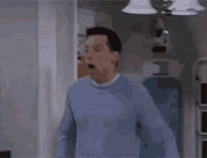 a man in a blue sweater is standing in a room with his mouth open and his eyes closed .